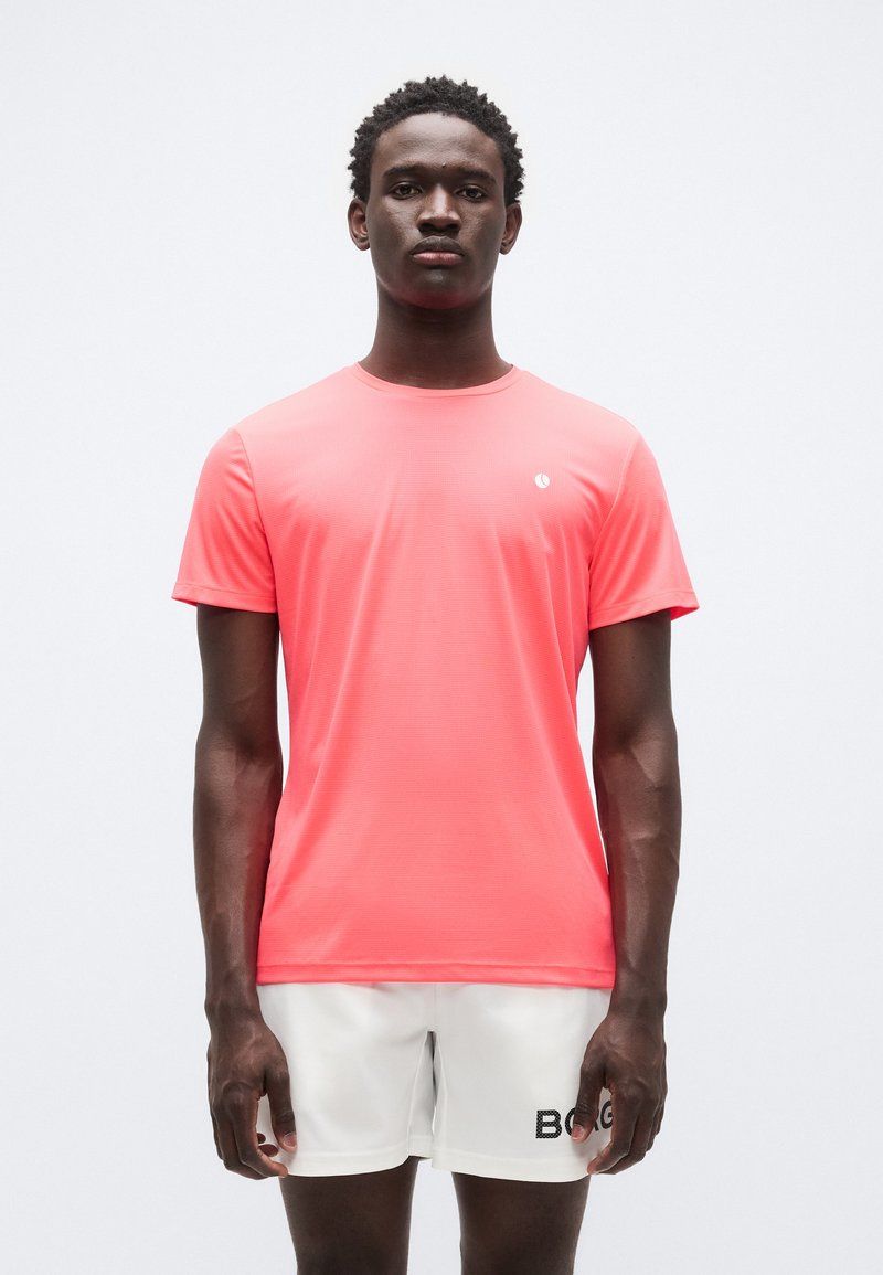 Αθλητική κοντομάνικη μπλούζα σε φωτεινή κοραλλί από ύφασμα που απομακρύνει την υγρασία. Διαθέτει μικρό λογότυπο στο αριστερό στήθος.