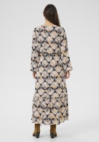 Maxikleid mit langen Ärmeln aus schwarzem Stoff mit einem Palmenblattmuster in Beige und Orange. Das Kleid hat einen gestuften Saum und eine taillierte Taille.