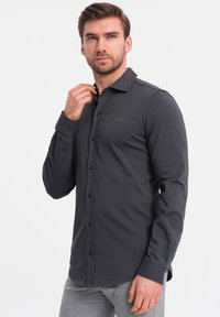 Grijze lange mouwen shirt met een button-up ontwerp, een klassieke kraag en een subtiel geborduurd logo op de borst. Soepele stof met een losse pasvorm.