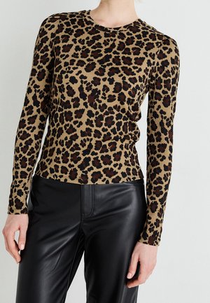 Kobieta ubrana w dopasowaną, długorękawową bluzkę w panterkę, zestawioną z wysokim stanem czarnych skórzanych spodni, stojąca na tle jednolitego tła.