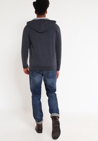 Felpa con cappuccio blu in tessuto morbido, con una vestibilità rilassata. Abbinata a jeans blu e stivali marroni scuri, con orlo risvoltato.
