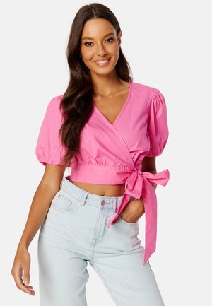 Haut rose à manches ballons avec un nœud à la taille, fabriqué en tissu lisse. Associé à un jean taille haute bleu clair.
