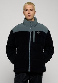 Pufferjakke med svart og grå fargekombinasjon, quiltet design, høy krage og frontglidelås med liten logo på brystet.