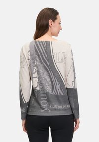 Pullover-Pullover in einer Mischung aus Beige und Grau, mit abstrakten Grafiken und Textmustern. Lange Ärmel und Rundhalsausschnitt.