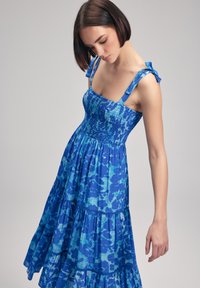 Abito estivo blu a più strati con corpino arricciato e spalline in nastro. Presenta un motivo floreale in diverse tonalità di blu. Tessuto leggero.
