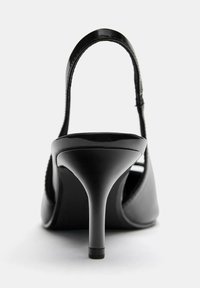 Čierne lakované vysoké podpätky sandále so štíhlym remienkom okolo členka a zúženým podpätkom, s hladkým povrchom a minimalistickým dizajnom.