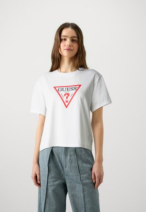 Biela bavlnená tričko s trojuholníkovou červenou a čiernou grafikou, ktorá zobrazuje "GUESS" a otáznik, krátke rukávy a voľný strih.