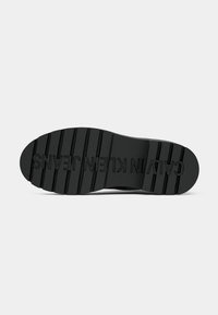 Soletta di scarpa in gomma nera con scanalature verticali e logo "CALVIN KLEIN JEANS" in rilievo, caratterizzata da una punta arrotondata e un tacco piatto.