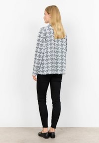 Szary kardigan w wzór houndstooth, luźny krój, długie rękawy i okrągły dół, połączony z czarnymi skinny spodniami i czarnymi butami.