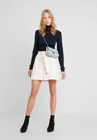 Marinblå polokrage, krämfärgad minikjol med framskjutna knappar och knytbälte, grå texturerad axelväska och svarta ankelstövlar fulländar outfiten.