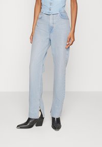 Jeans de mezclilla azul claro con piernas rectas, con aberturas en los laterales en el dobladillo y diseño de cintura alta. Combinados con botines negros de tacón puntiagudo.