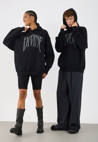 Hanorace negre cu glugă, având inscripția "DIVINE" în sclipici argintiu, asociate cu pantaloni scurți tip ciclism negri și pantaloni largi; model purtând cizme până la genunchi.