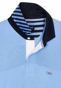 Polo bleu clair avec un tissu texturé, col contrastant en marine et doublure intérieure rayée. Présente des boutons blancs et un petit logo.