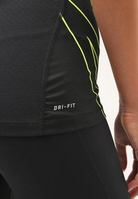 Gros plan sur une personne portant des vêtements de sport noirs Dri-FIT avec des rayures jaune néon sur le côté et des détails de couture visibles.