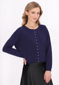 Pulover scurt de culoare bleumarin, confecționat din material tricotat, cu decolteu rotund, mâneci lungi și nasturi decorativi din perlă pe partea din față.