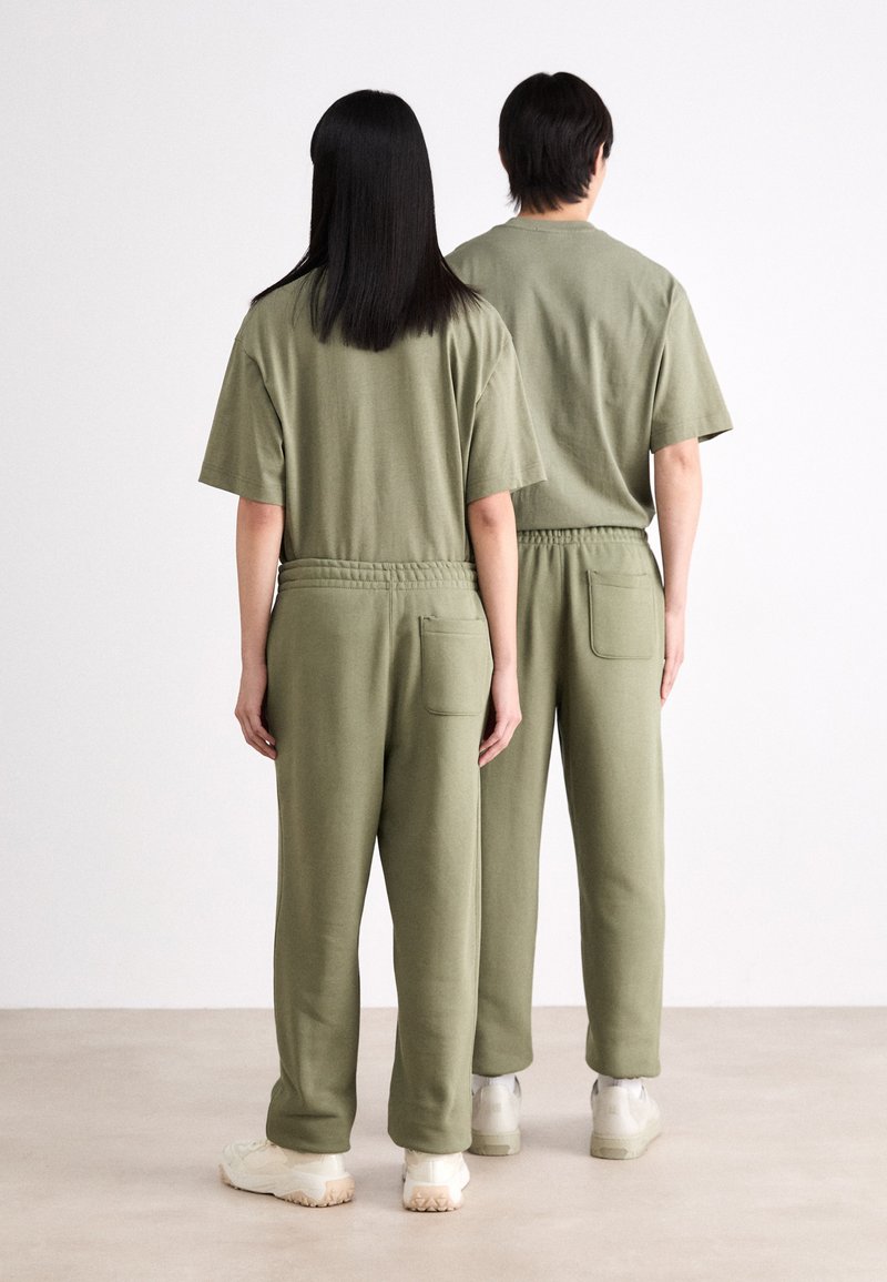 Olijfgroene bijpassende t-shirts en joggers met elastische taille, voorzien van zijzakken en een ontspannen pasvorm, gedragen door twee personen gezien van achteren.