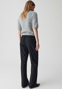 Pull court en peluche gris à manches courtes associé à un pantalon noir ajusté. L'ensemble présente une coupe décontractée et une texture de tissu lisse.