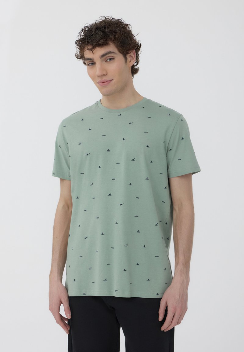 T-shirt verde chiaro a maniche corte con un motivo di uccelli neri sparsi. Realizzato in un tessuto morbido e traspirante con scollo a girocollo.