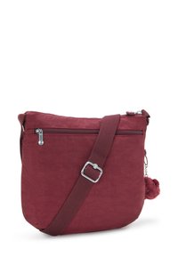 Maroon shoulder bag made of soft fabric, featuring a zippered top and front pocket, with a textured pom-pom accent and adjustable strap.