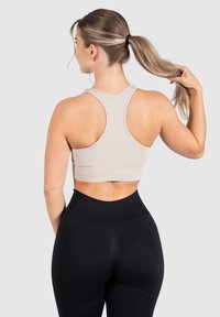 Beige geribbelde sport-beha met een racerback ontwerp, gecombineerd met hoge zwarte leggings. Glad textuur en aangesloten silhouet.