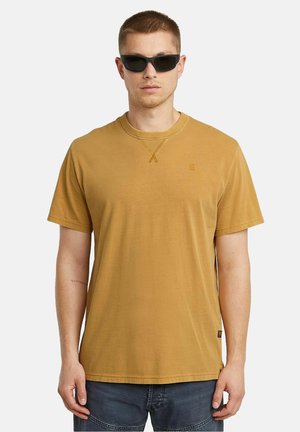 Mosterdgele T-shirt met korte mouwen en een ronde halslijn, voorzien van een zijlabel. Gemaakt van katoen, met stikaccenten bij de halslijn.