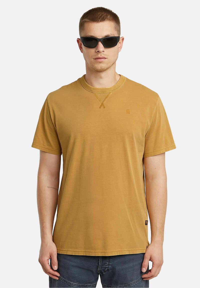 T-shirt giallo senape a maniche corte con scollatura tonda e etichetta laterale. Realizzato in cotone, presenta dettagli di cucitura sullo scollo.