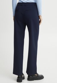 Marina vida byxor med vida ben har en slät tygkvalitet, bakfickor och en skräddarsydd midja. Kombineras med svarta loafers för en enhetlig look.