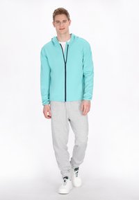 Felpa zip blu chiara con zip blu scuro, abbinata a pantaloni della tuta grigi e sneakers bianche. Tessuto morbido con una vestibilità comoda.