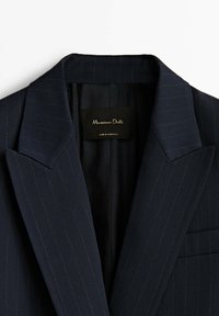 Blazer bleu marine foncé à fines rayures, avec larges revers et une étiquette Massimo Dutti visible à l'intérieur du col.
