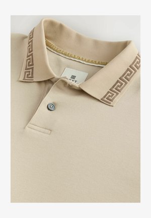 Beige poloshirt met een gestructureerde kraag die een donkerbruine Grieks sleutelmotief heeft; sluiting met één knoop; gladde stoftextuur.