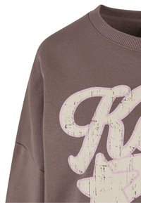 Felpa marrone con colletto a coste che mostra una grande grafica consumata in crema e rosa chiaro con la parola "Rock" e una stella.
