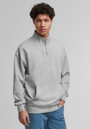 Sweat à zip gris clair avec un col haut et une poche avant. Présente une coupe loose et des poignets côtelés, fabriqué en tissu doux.