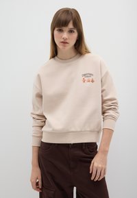 Felpa beige con scollo rotondo, polsini e orlo a costine. Presenta un ricamo con la scritta "Cookies di Natale" e elementi festivi.