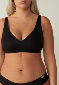 Svart bralette med v-ringad design, tillverkad av mjukt tyg, med breda remmar och en slät, sömlös finish.