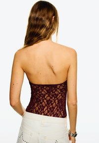 Burgundowa koronkowa bluzka bez ramiączek z marszczeniem, o dopasowanym kroju. Noszona z białymi szortami dżinsowymi z dekoracyjnymi akcentami.