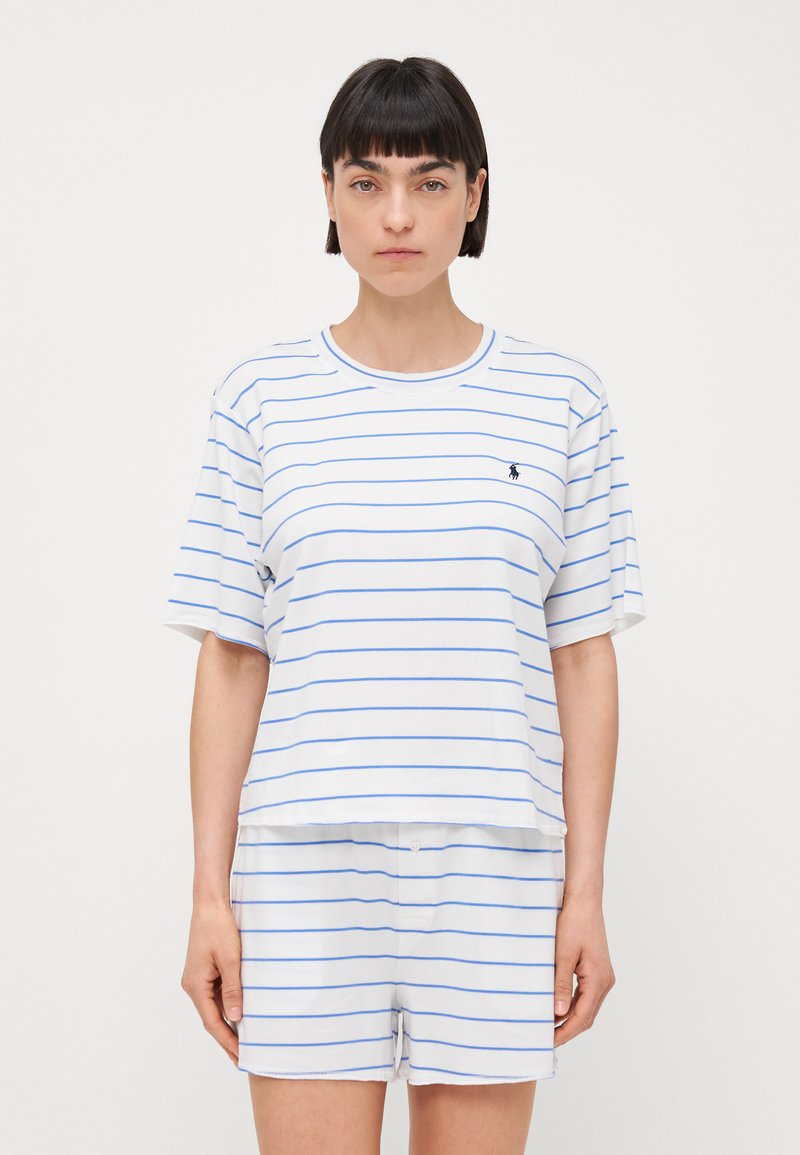 Wit gestreept T-shirt met blauwe lijnen en korte mouwen, gecombineerd met witte shorts. Het materiaal lijkt zacht en casual, met een logodetail.