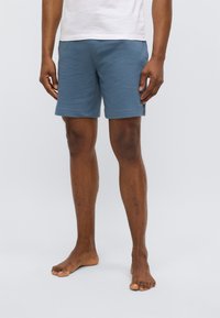 Blue textured swim shorts with a relaxed fit, featuring a waffle pattern and side pockets. Worn barefoot on a neutral background.