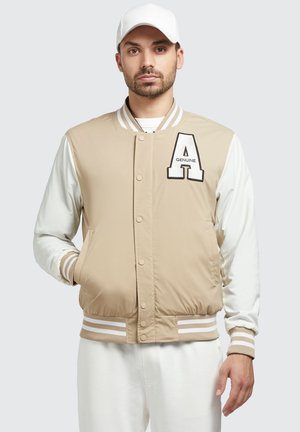 Beige bomber jacket with white sleeves, featuring a letter "A" patch, snap buttons, and striped ribbed cuffs and hem.