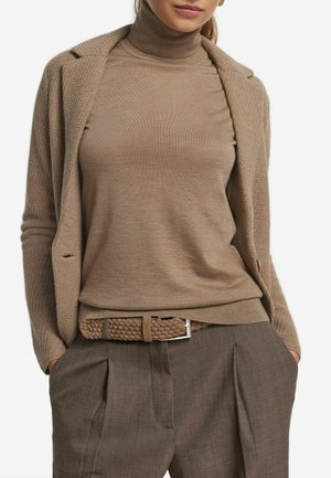 Brauner Strickrollkragenpullover unter einem strukturierten beigen Blazer, kombiniert mit braunen gefältelten Hosen und einem geflochtenen braunen Gürtel mit silbernen Beschlägen.