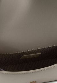 Interieur van een beige leren handtas met een gladde textuur, voorzien van een gevoerde voering in bruine tinten en een merkteken in goudkleur.