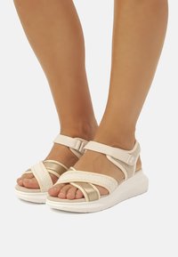 Sandali con zeppa beige dotati di cinture testurizzate, fibbia regolabile e suola ammortizzata. Presentano dettagli intrecciati e un design traspirante.