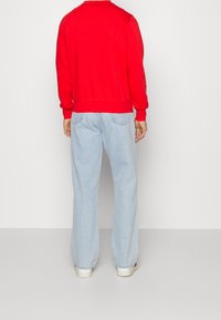 Rode crewneck sweatshirt met geribbelde manchetten en onderrand, gecombineerd met lichtblauwe wijde spijkerbroek met achterzakken en een ontspannen pasvorm.