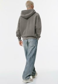 Gray hooded sweatshirt with loose fit, paired with light blue striped wide-leg pants. The outfit features ribbed cuffs and side pockets.
