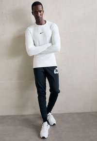 Pitkähihaista valkoista urheilu puseroa, jossa on musta Nike logo, yhdistetty mustiin housuihin, joissa on valkoinen Nike painatus, ja urheilullisiin valkoisiin kenkiin.
