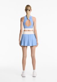 Blue sports crop top with a back cutout, paired with a blue skirt featuring a white waistband and pleated design. Lightweight fabric.