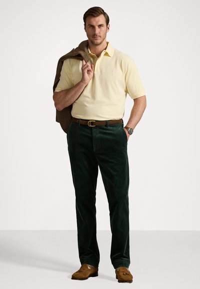 Cămașă polo de culoare galben pal, combinată cu pantaloni din catifea grosieră de culoare verde închis. Curea din piele maro și mocasini maro asortați. Ținută smart-casual.