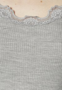 Grå randig topp med en skulpterad spetskrage. Tyget har en mjuk textur, med subtila vertikala linjer och fint spetsdetaljer.