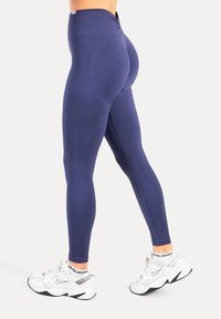Leggings bleu marine longueur intégrale avec une ceinture côtelée et une texture lisse, assortis à des chaussures de sport blanches avec des accents argentés.