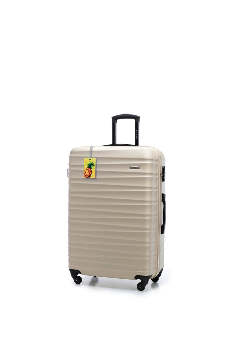Maleta rígida beige con asa retráctil negra, cuatro ruedas, asa lateral y una etiqueta de equipaje colorida con piña.