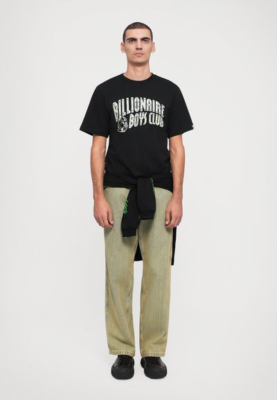 Schwarzes Baumwoll-T-Shirt mit weißem und grünem "Billionaire Boys Club"-Grafik. Kombiniert mit hellgrünen gestreiften weit geschnittenen Hosen und schwarzen Turnschuhen.